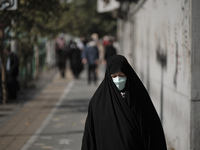 An Iranian veiled woman wearing a protective face mask walks along an avenue to the University of Tehran for taking part the Friday prayers...