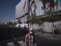 An Iranian man wearing a protective face mask walks under a portrait of Iran’s Supreme Leader Ayatollah Ali Khamenei while walking along an...