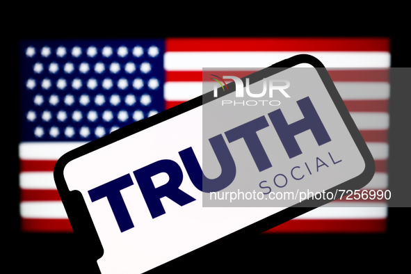 TRUTH Social logo is seen displayed on a phone screen with Amercan flag displayed on a laptop screen in the background in this illustration...