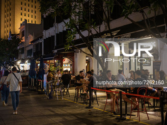 People seated at tables in groups of 2 as mandated by Covid-19 safety restrictions drink at bars in Singapore on Saturday, 23 October, 2021....