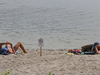 A men sunbathe on Verbne lake shore next to the caution “Swimming is temporarily prohibited” board. Several people were deadly infected with...