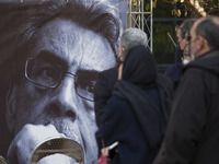 Iranian people stand next to a portrait of Iranian cartoonist Kambiz Derambakhsh while attending a funeral for Derambakhsh out of the Irania...