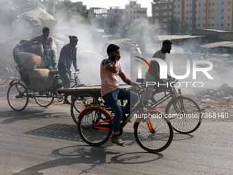 People make their move as garbage fire creates toxic smoke beside a road near the old Buriganga river channel at the Keraniganj area in Dhak...