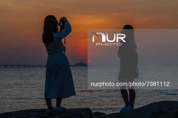 Two young ladies take pictures of themselves in front of the sunset near Hong Kong International Airport. 