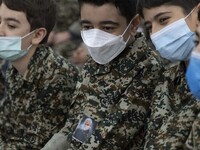 Iranian young boys in military uniforms wearing protective face masks as one of them pastes a portrait of the Iranian top IRGC commander, Ge...