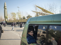 An Iranian schoolboy sits in a vehicle as it drive past the Iranian Qiam short-range surface-to-surface ballistic missile (L), Solid-propell...
