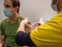 A man wearing facemask is getting the Covid shot vaccine by a medical health care worker in the vaccine booth pod. Vaccination center in Ein...
