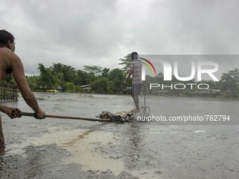 An Indian man helps a boy on a makeshift boat in crude oil on flood waters at Duliajan, about 500kms east of the capital city of Guwahati in...