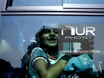 A girl smiles through a window in a bus going to the Piraeus railway station, on September 5, 2015.  The chartered by the Greek government p...