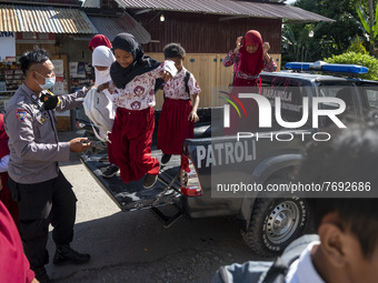 A police officer helps unload students from the patrol car that transported them to take part in the COVID-19 vaccine at SD Negeri Porame, P...
