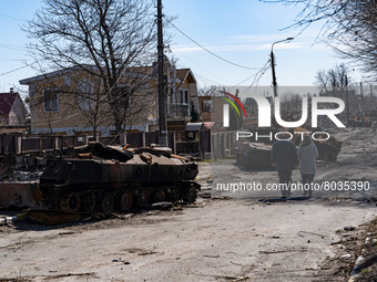 BUCHA, UKRAINE - APRIL 7, 2022 - A man and a woman walk along a street lined with destroyed military vehicles after the liberation of the ci...