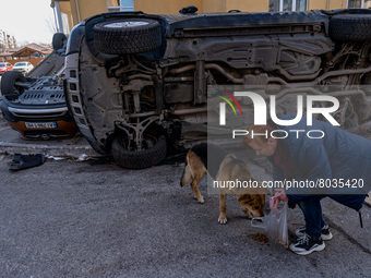BUCHA, UKRAINE - APRIL 7, 2022 - A woman feeds a dog near an overturned car after the liberation of the city from Russian invaders, Bucha, K...