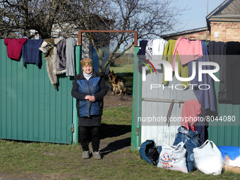 KYIV REGION, UKRAINE - APRIL 07, 2022 - A local woman stands by the fence hung with clothes as part of the humanitarian aid for the people i...