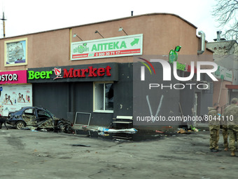 KYIV REGION, UKRAINE - APRIL 07, 2022 - A destroyed car parked outside a damaged store marked with 