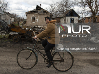 A woman rides a bicycle against the background of a destroyed military truck in the village of Andriyivka, Kyiv region, on April 12, 2022....