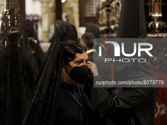A penitent dressed in black from the Maria Santisima de la Concepcion Brotherhood helps to put an earring to a woman with a face mask during...