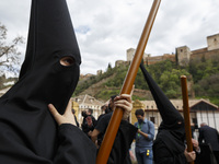 A penitent dressed in black of Maria Santisima de la Concepcion Brotherhood walks with a view of the Alhambra monument during the Maundy Thu...