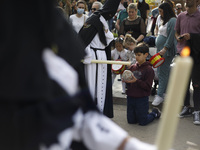 A child collects wax from a candle of a penitent from the Escolapios Brotherhood during the Good Friday in Granada, Spain, on April 15, 2022...
