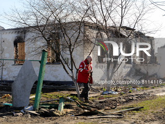 KYIV REGION, UKRAINE - APRIL 7, 2022 - A Ukrainian Red Cross Society worker walks past a destroyed house in a town liberated from Russian in...