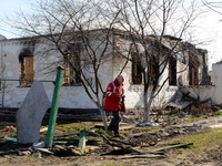 KYIV REGION, UKRAINE - APRIL 7, 2022 - A Ukrainian Red Cross Society worker walks past a destroyed house in a town liberated from Russian in...