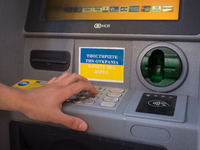 A man is typing on an ATM that writes on a piece of paper ‘Support Ukraine, make a donation’ in Athens, Greece on May 9, 2022. (