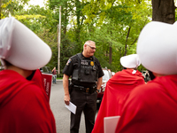A Chevy Chase Village police officer speaks with demonstrators dressed as handmaids from the Handmaid's Tale before they walk to the Chevy C...