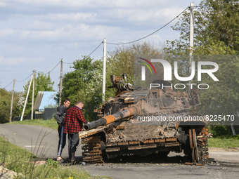 Local men explore burned tank on the street in Zahaltsi village near Kyiv, Ukraine, ​May 13, 2022. (
