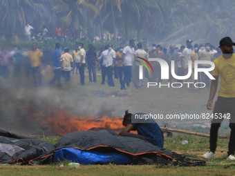 A Sri Lankan anti-government protester tries to retrieve belongings from his tent that is on fire as pro-government protesters look on after...