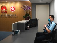 A police officer sits at the reception for the Office of the Chief Executive Elect next to the National Emblem of the People’s Republic of C...