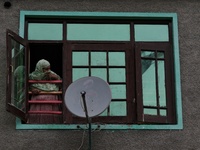 A woman watches from the window of her house as senior political leader and Former Deputy Chief Minister of Jammu and Kashmir Muzaffar Hussa...