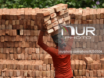 A Laborer unloads bricks from a cargo ship at the Kamrangirchar area in Dhaka, Bangladesh on May 18, 2022. (