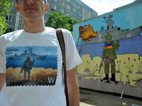 ZAPORIZHZHIA, UKRAINE - MAY 19, 2022 - A man in a T-shirt with the famous postage stamp stands before a mural by street artist Denys Antiuko...