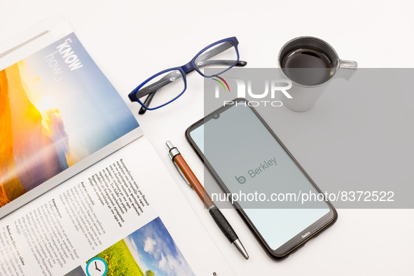 In this photo illustration a berkley Insurance logo seen displayed on a smartphone screen on a desk next to a cafe, a pen, glasses and a mag...