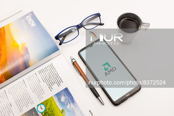 In this photo illustration an Advanced Micro Devices (AMD) logo seen displayed on a smartphone screen on a desk next to a cafe, a pen, glass...