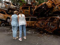 Two women watch burned cars on a parking destroyed by bombardment on June 14, 2022 in Irpin, Ukraine.  The cars were collected from the stre...