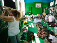 Volunteers weave a camouflage net from old fabrics in the local school gym. (