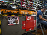 A man awaits for customers in a shoe shop with a sign displaying the acceptance of Bitcoin as a payment method on June 15, 2022 in San Salva...