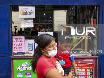 A woman carrying a child walks next to a sign displaying the acceptance of Bitcoin as a payment method on June 15, 2022 in San Salvador, El...