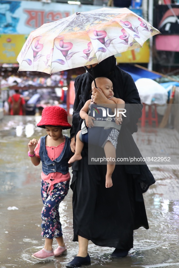 A woman walks thorugh a light rain with her children in Dhaka, Bangladesh on June 17, 2022. 
