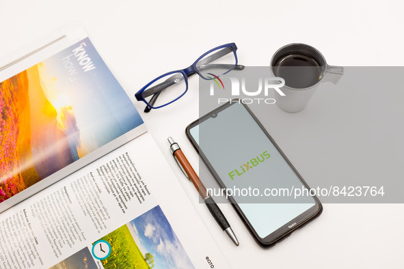 In this photo illustration a FlixBus logo seen displayed on a smartphone screen on a desk next to a cafe, a pen, glasses and a magazine in A...