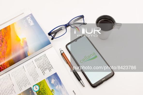 In this photo illustration a Cellana logo seen displayed on a smartphone screen on a desk next to a cafe, a pen, glasses and a magazine in A...
