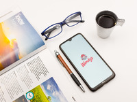 In this photo illustration a Wendy’s Company logo seen displayed on a smartphone screen on a desk next to a cafe, a pen, glasses and a magaz...