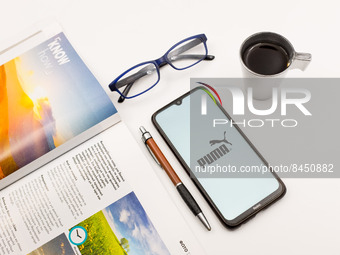 In this photo illustration a Puma logo seen displayed on a smartphone screen on a desk next to a cafe, a pen, glasses and a magazine in Athe...