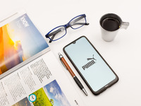 In this photo illustration a Puma logo seen displayed on a smartphone screen on a desk next to a cafe, a pen, glasses and a magazine in Athe...