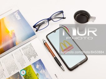 In this photo illustration a McDonald's logo seen displayed on a smartphone screen on a desk next to a cafe, a pen, glasses and a magazine i...