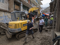 Iranian men walk past a bulldozer working on a street covered with mud after flash flooding in the flooded village of Imamzadeh Davood in th...
