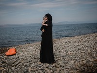 A women holds her child while looking back towards the sea she and her family just crossed from Turkey, in Lesbos, Greece, on September 26,...