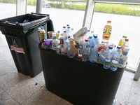 A full garbage bin with plastic bottles on top, as the passenger traffic exceeds the hourly operation capacity of the airport and due to lab...