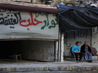 Two of the men sitting beside an advert written on the wall in Aleppo, Syria october 27,2015. The text on the wall reads in Arabic, 