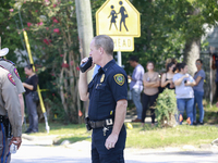 An officer communicates orders while worried parents wait behind him.  (
